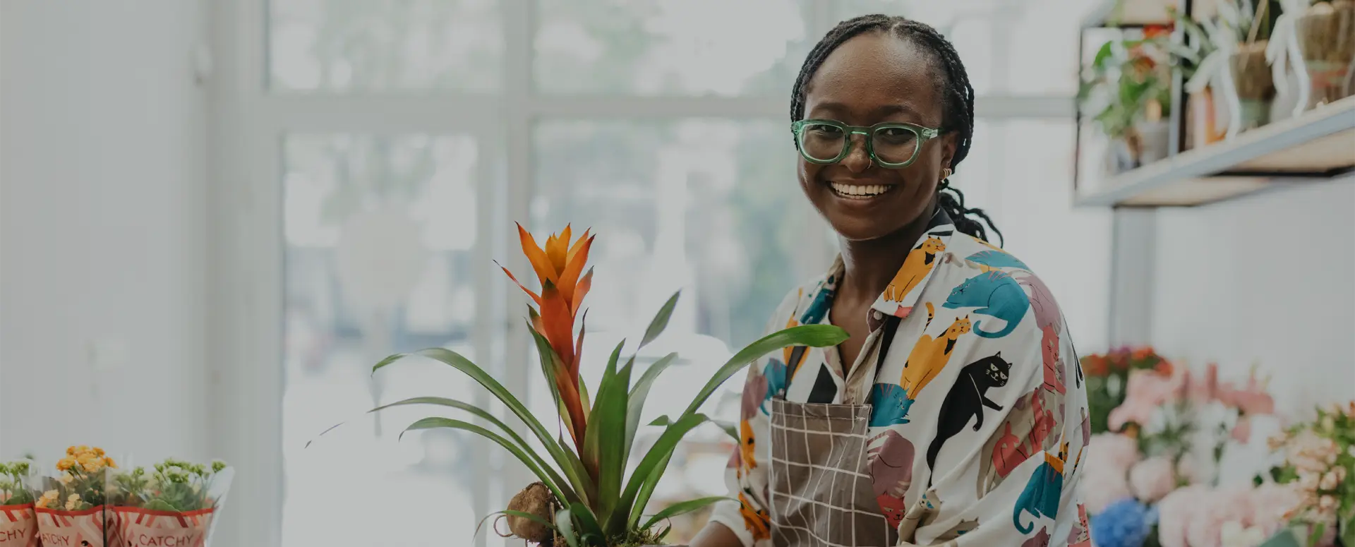 A smiling woman standing in a flower shop holding a clipboard.