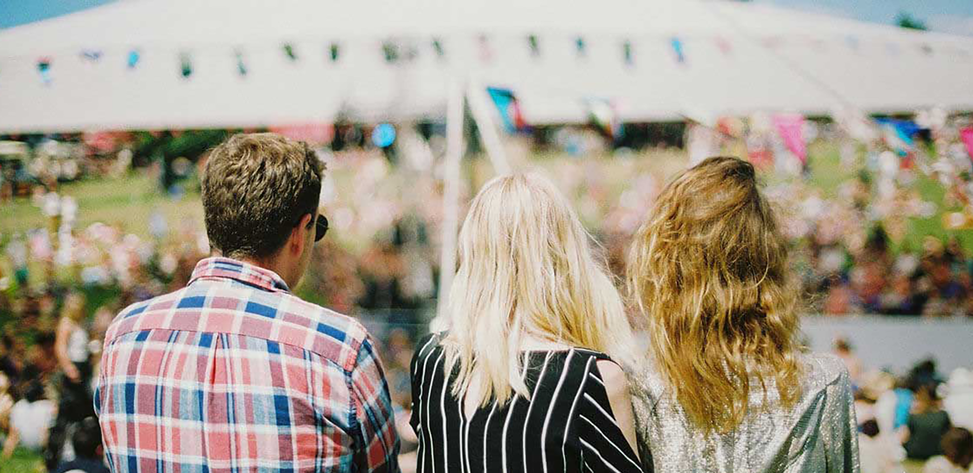 A trio of people standing in front of an out-of-focus tent and crowd.