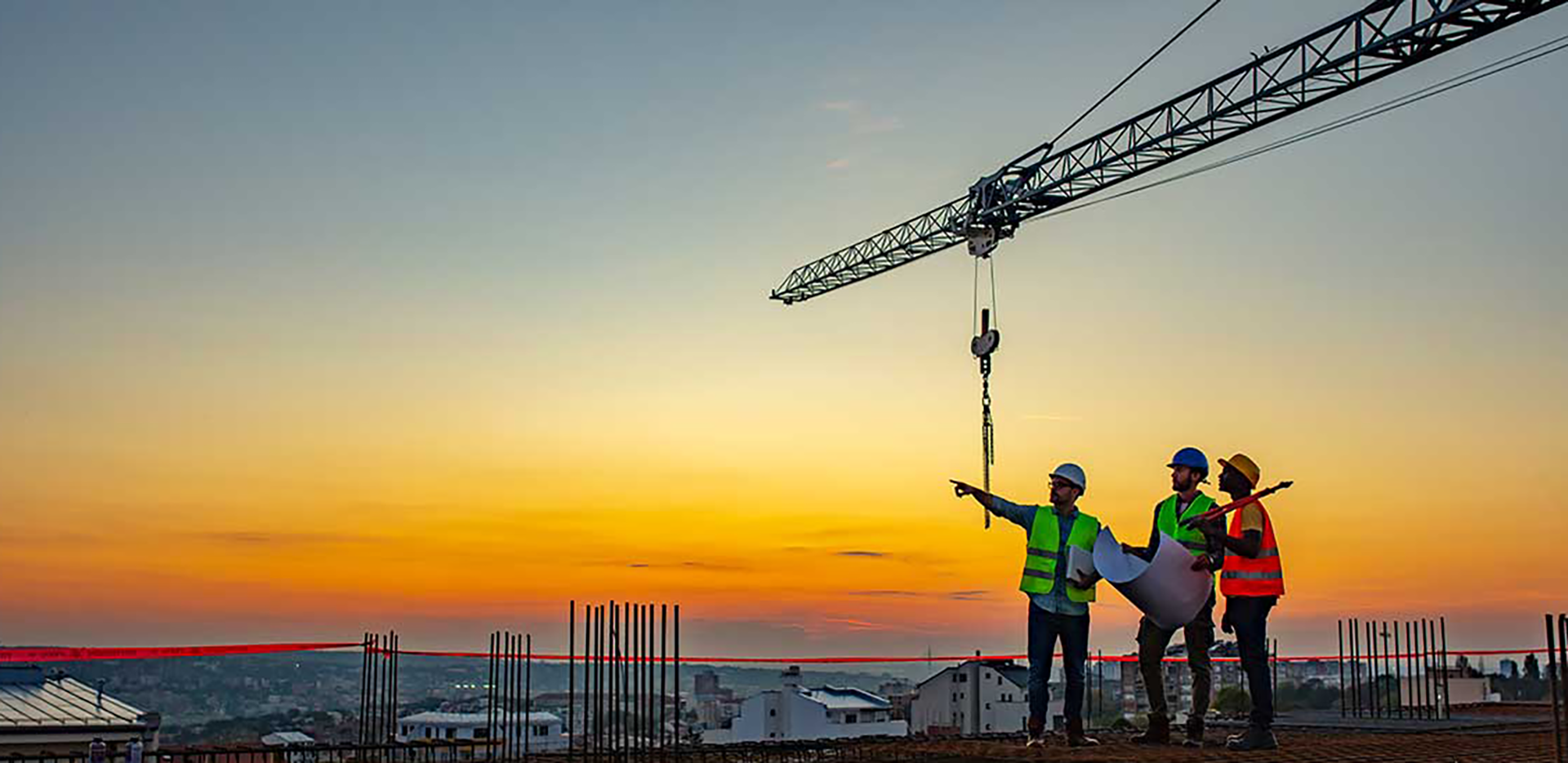 A trio of construction workers looking at blueprints standing in front of a crane.