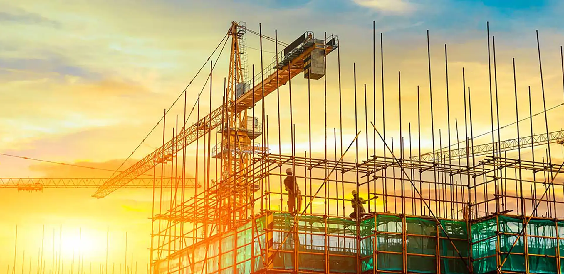 Two construction workers on scaffolding with cranes in the background.