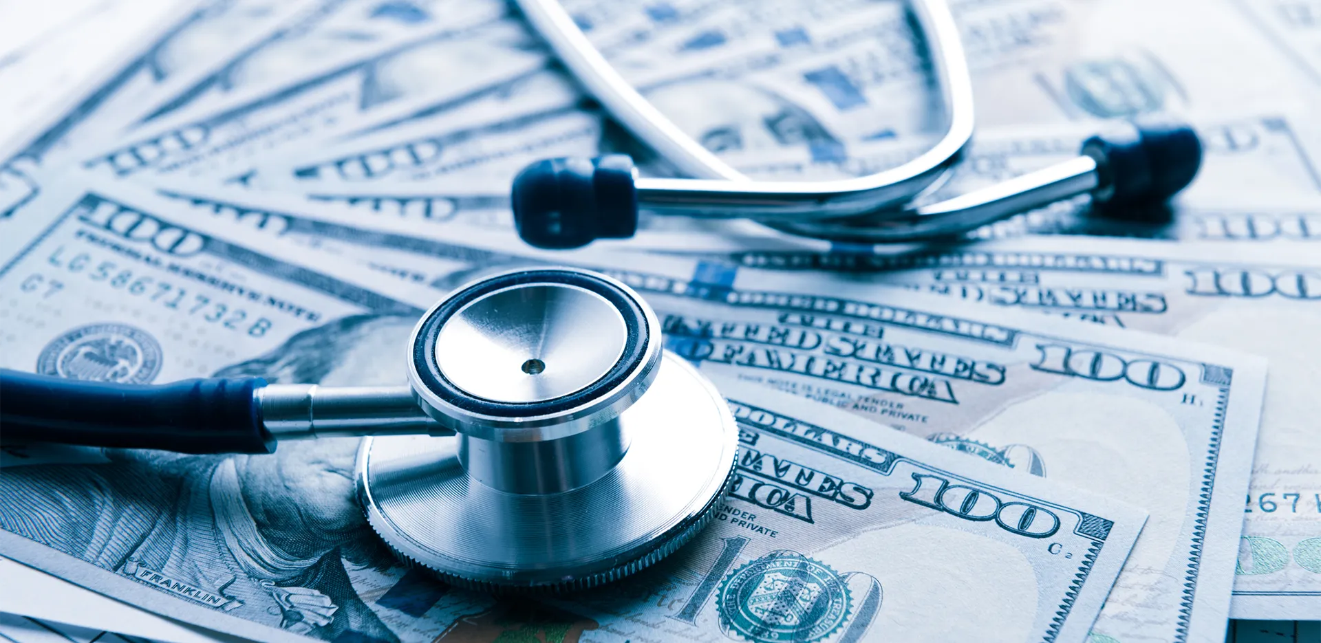 A pile of 100 dollar bills with a stethoscope on top of them.