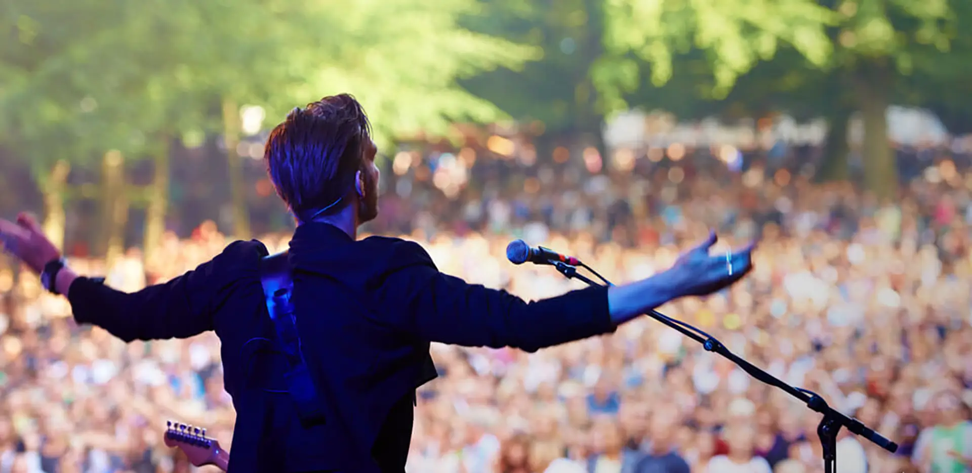 A musician standing with arms outstretched in front of a crowd.
