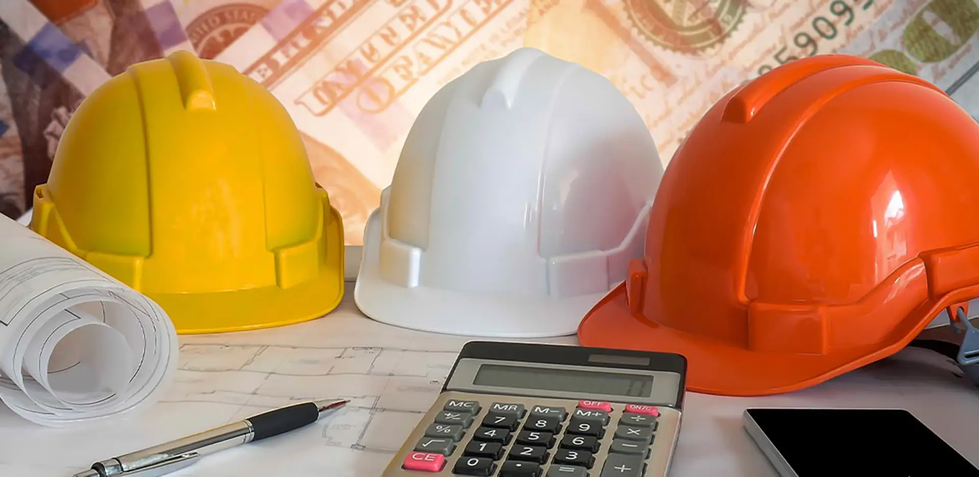 A trio of hard hats, a blueprint, and a calculator.
