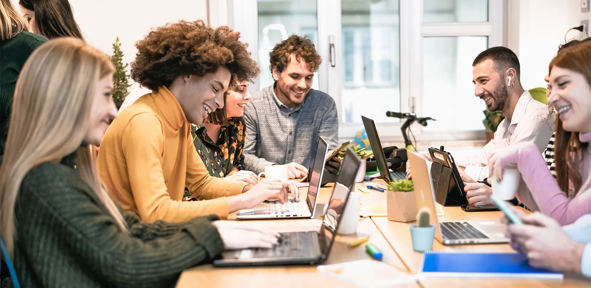 A group of young professionals talking and laughing while working at their computers.