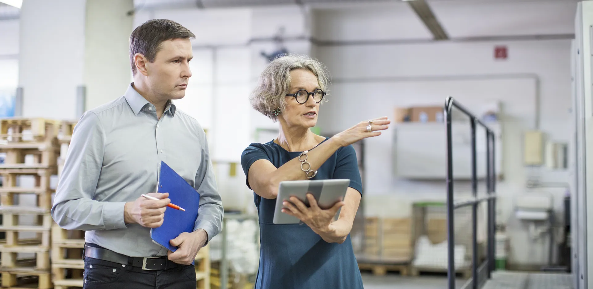 A person with a clipboard and a person with a tablet conduct a workplace inspection.