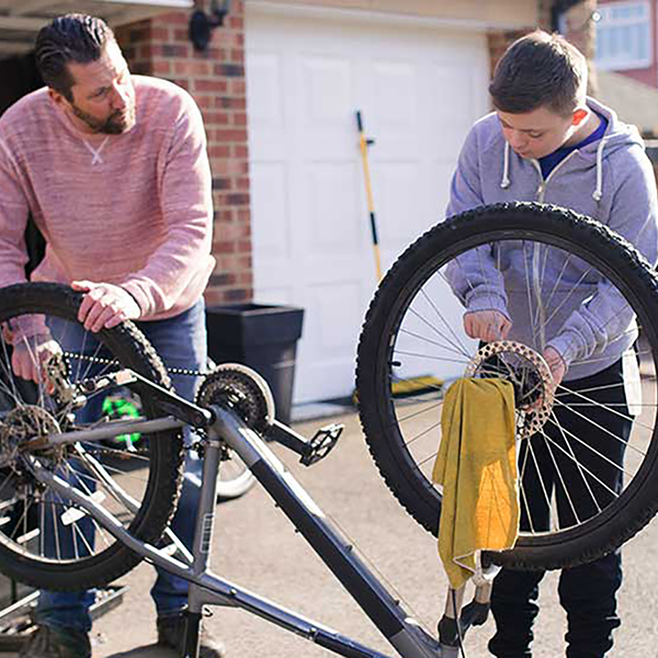 A father and son working on repairing a bicycle in their driveway.