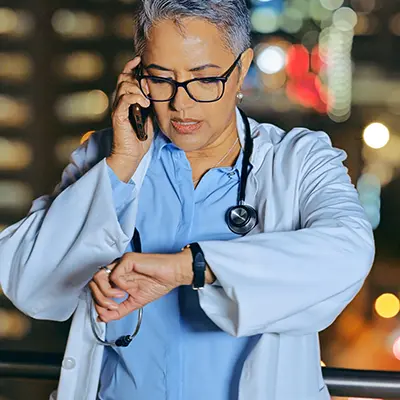 A doctor talking on a mobile phone and looking at her watch.