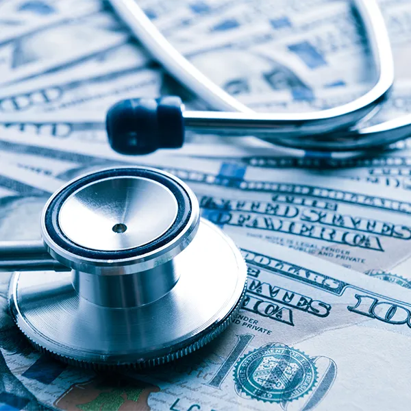 A pile of 100 dollar bills with a stethoscope on top of them.