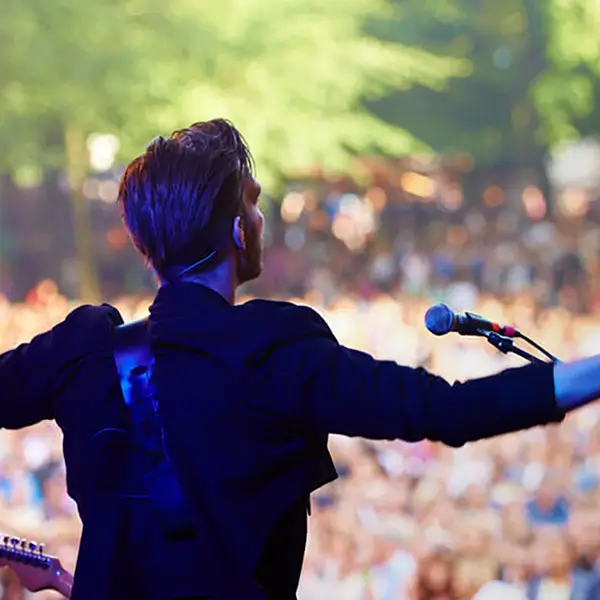A musician standing with arms outstretched in front of a crowd.