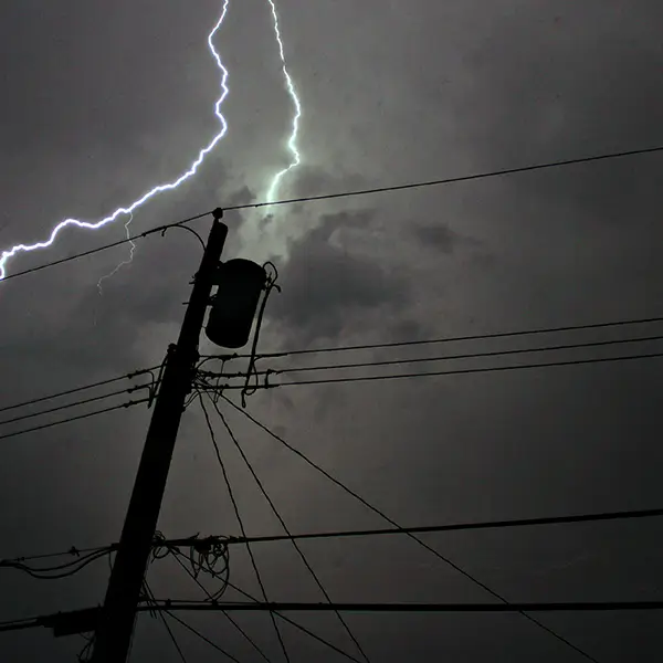 Powerlines backlit by lightning against a stormy sky.