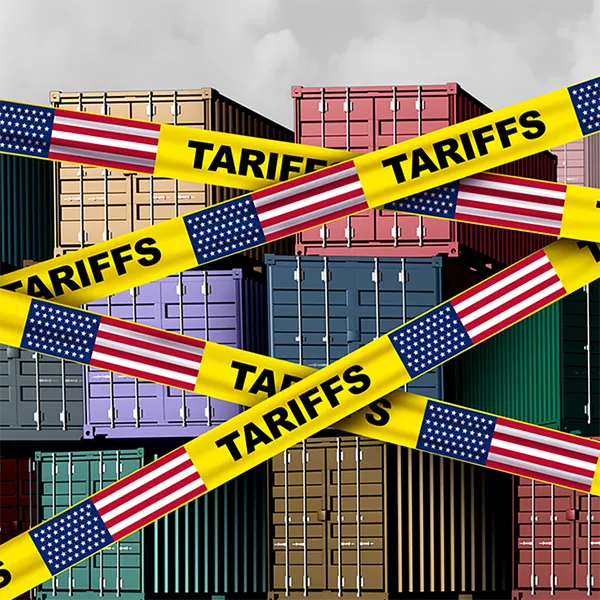 Yellow tape with the word 'tariffs' and the American flag in front of stacks of shipping containers.