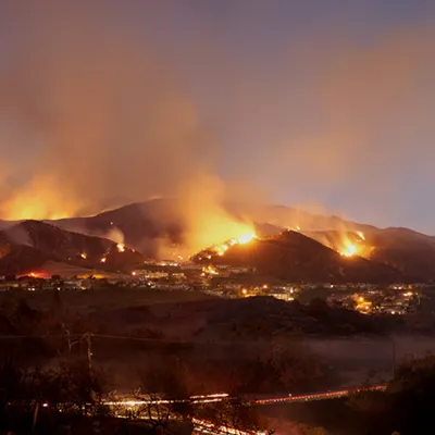An urban hillside covered in wildfires and smoke.