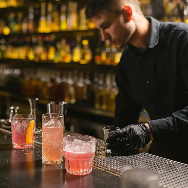A bartender wearing gloves prepares three cocktails.