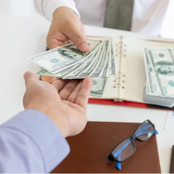 A person handing another person a stack of $100 bills.
