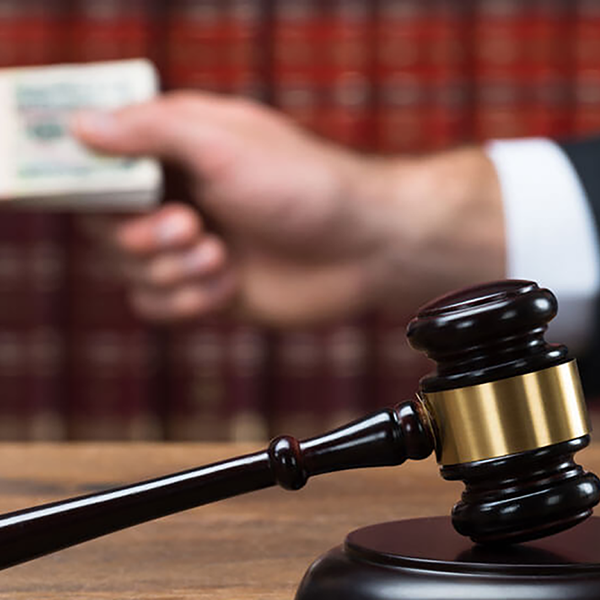 A judge's gavel and sounding block. In the background a stack of money changes hands.