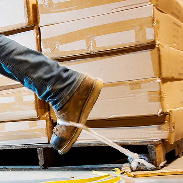 A construction worker tripping over a piece of tape next to a stack of boxes.