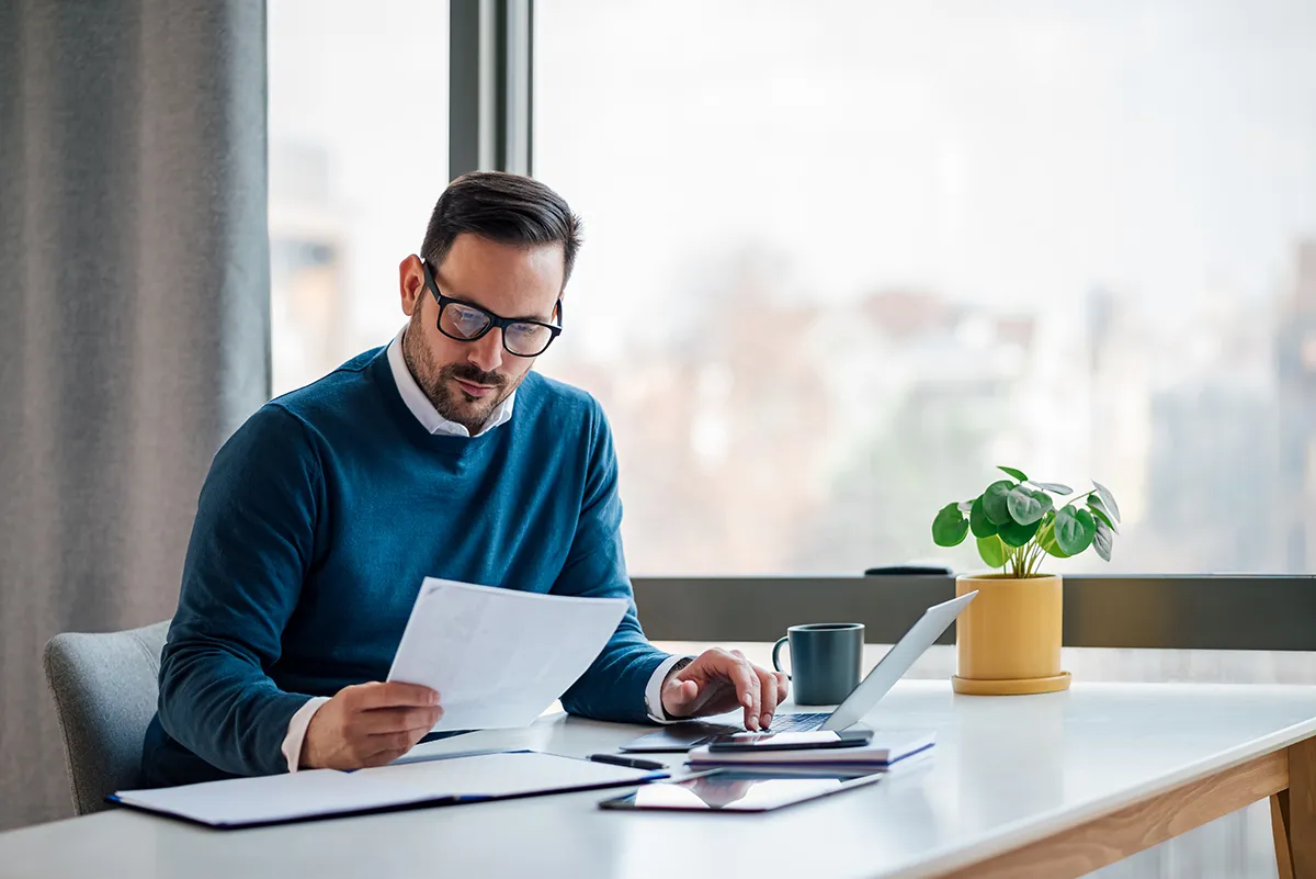a man wearing a sweater and glasses sitting at a desk reviewing paperwork