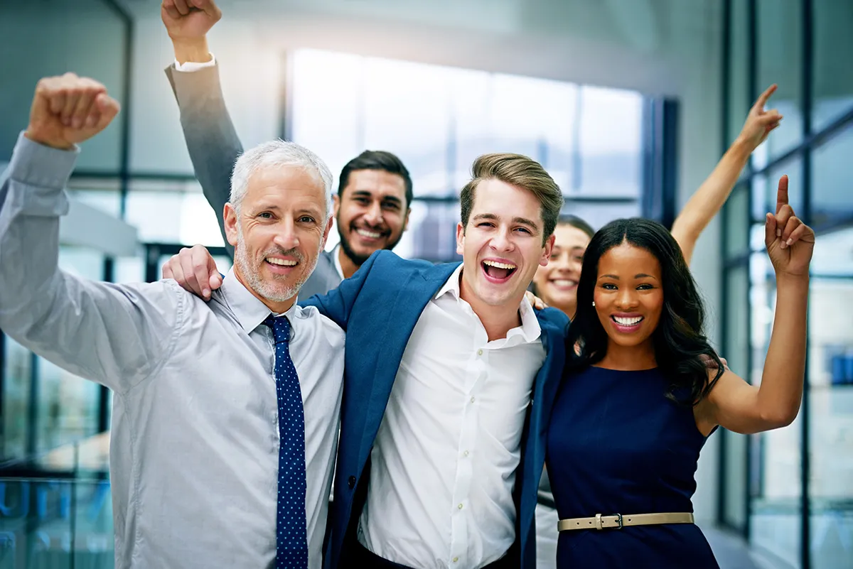 a group of happy co-workers embracing and holding their arms up in the air