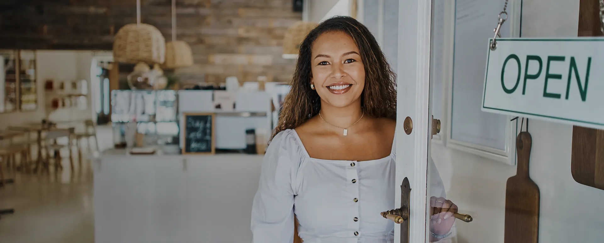 A smiling woman stand in the open doorway of her small business.