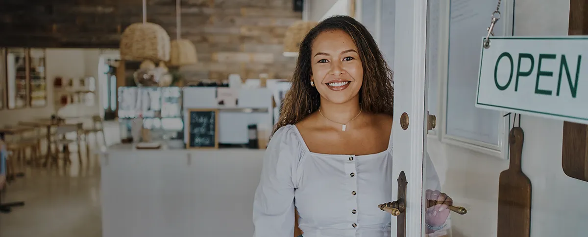 A smiling woman stand in the open doorway of her small business.