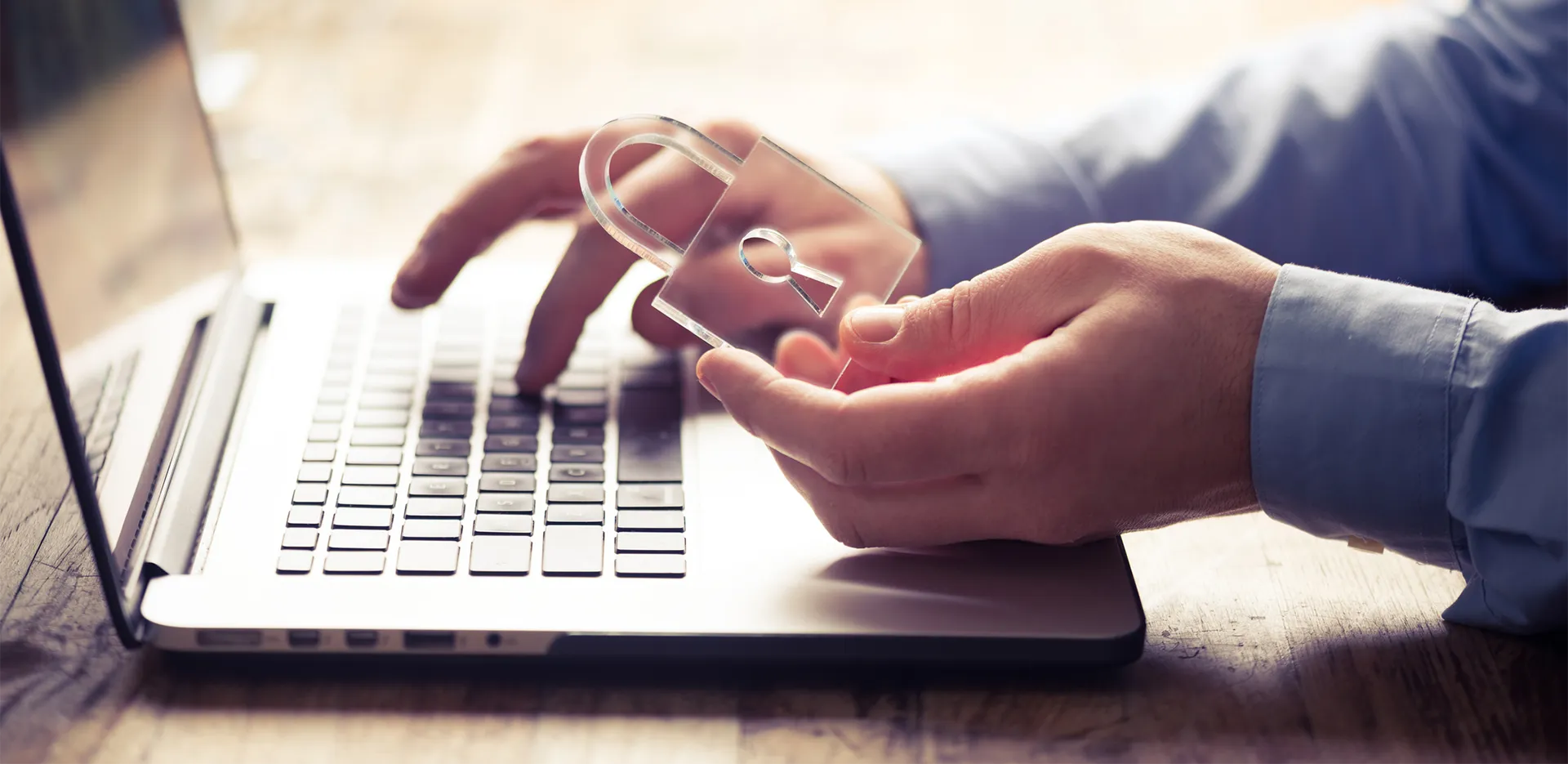 A person typing on a laptop computer. They're holding a transparent lock.