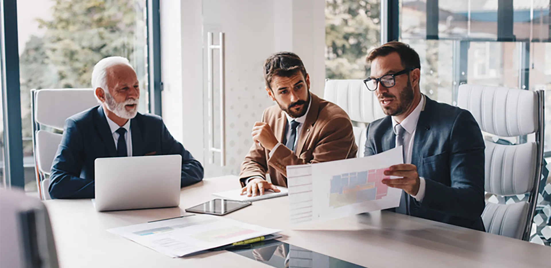 Three professionals wearing suits review a report.