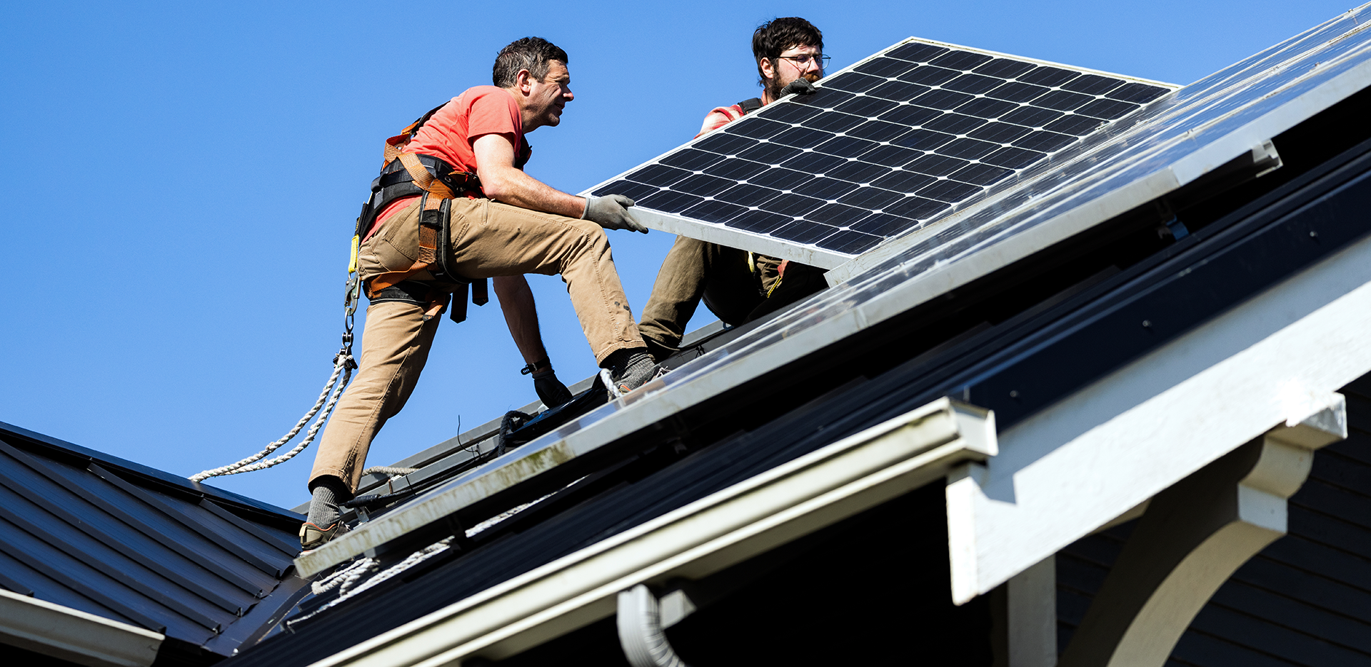 Two contractors install solar panels on the roof of a house.
