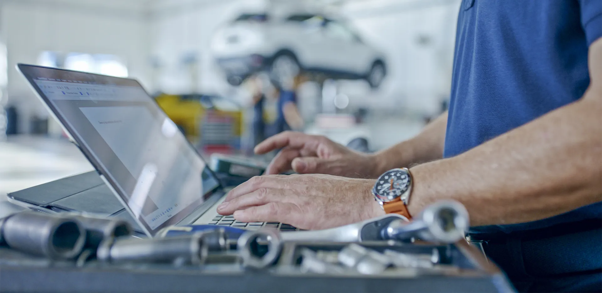 A person typing on their laptop computer surrounded by tools.