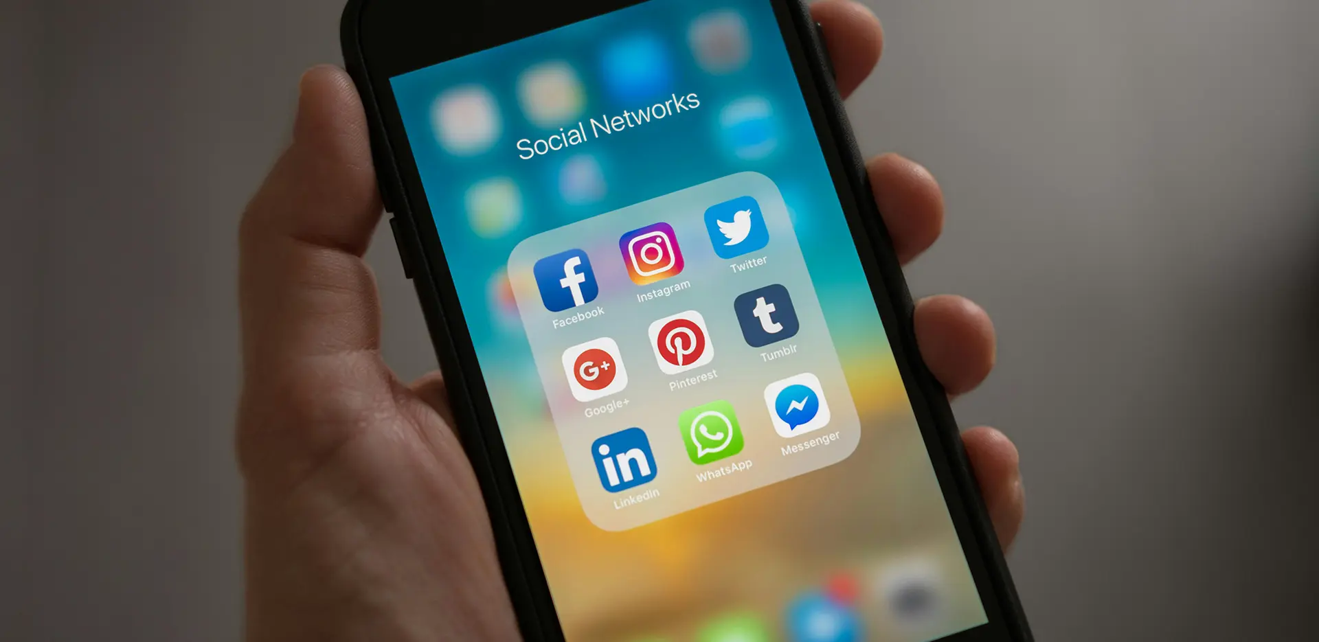 A mobile phone in a person's hand displaying social media app icons.