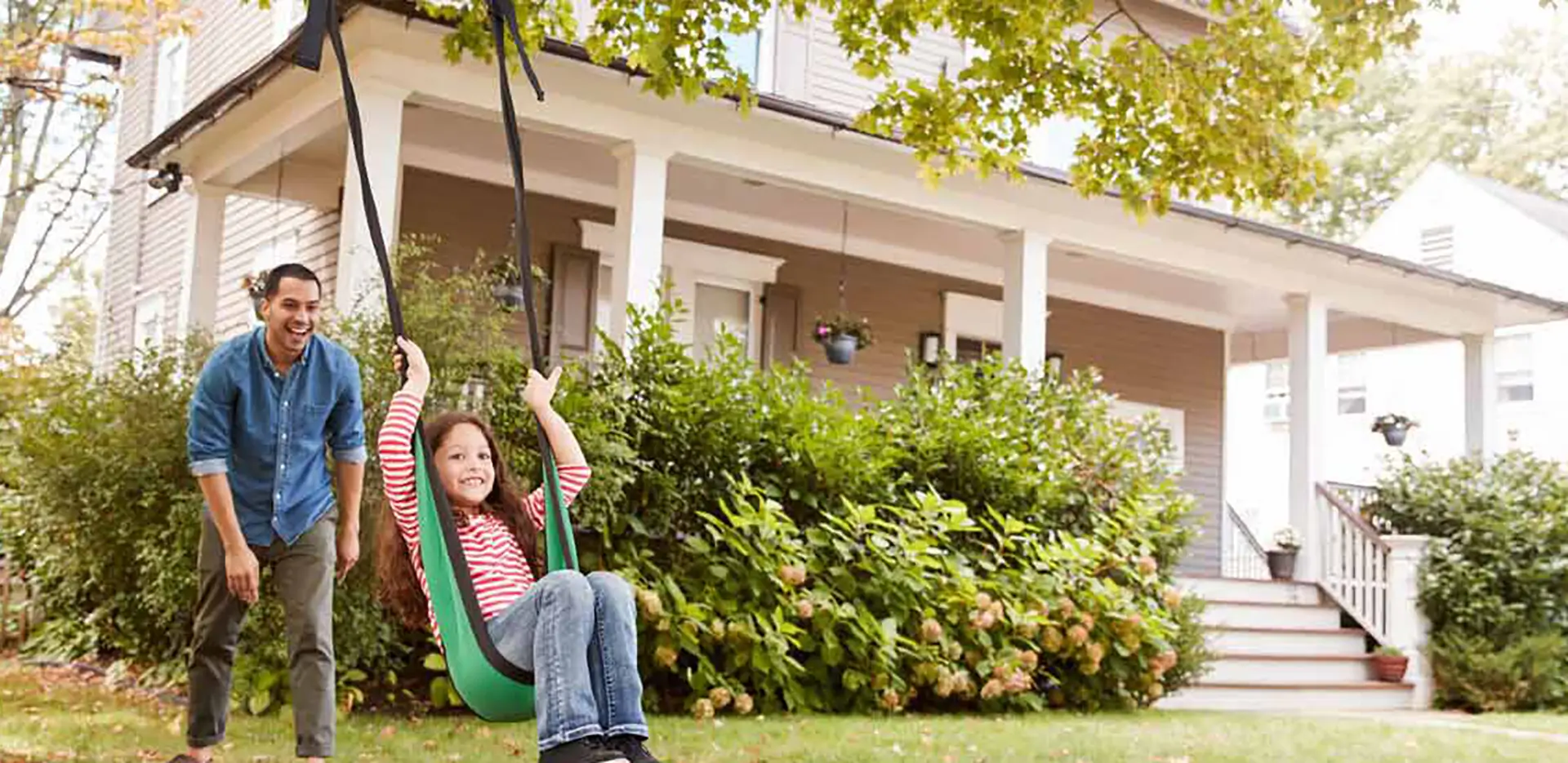 A father and child playing on a swing in their front yard.